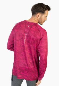 Pitkähihaisen urheilupaidan kirkkaan pinkki väri, jossa on teksturoitu kuvio. Paidassa on selässä Spider-logo ja erottuvat ompeluyksityiskohdat.