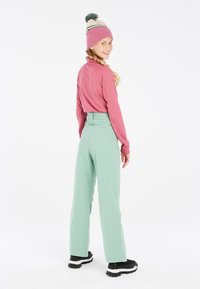 Roze langemouwtop, mintgroene hoge taille broek en een beanie met een pompon. Zwarte laarzen met witte zolen. Eenvoudig ontwerp, zachte textuur.