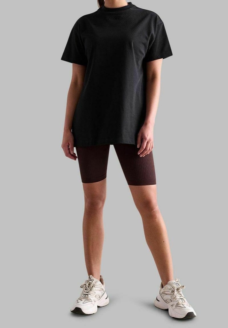 Zwarte katoenen t-shirt, oversized pasvorm, gecombineerd met gestructureerde bruine fietsbroek en witte sportschoenen met grijze accenten. Eenvoudig ontwerp, casual kleding.