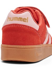 Czerwony zamszowy i siateczkowy sneaker z białymi akcentami i gumową podeszwą w kolorze gumy. Posiada pasek na rzep oraz złote logo "hummel" na pięcie.