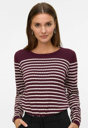 Pull rayé bordeaux et crème avec une texture côtelée, un col rond et des manches longues. Associé à un pantalon noir, l'ensemble est décontracté et confortable.