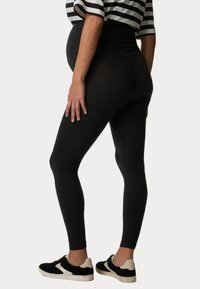 Czarne legginsy z wysokim stanem, wykonane z gładkiego, rozciągliwego materiału. W połączeniu z czarno-białymi sneakersami. Częściowo widoczny jest pasiastego top.
