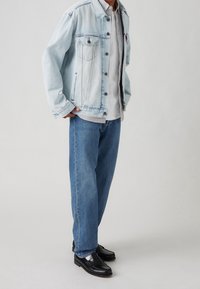 Ljust blå denimjacka med klassisk design, två bröstfickor, grå t-shirt under, ihopparad med vida blå jeans och svarta loafers.