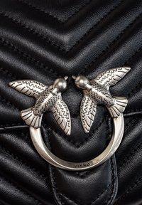 Zwarte gebsurde leren tas met een zilverkleurige metalen ring met twee vogelversieringen. Opvallend visgraatpatroon op het leren oppervlak.