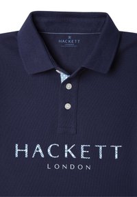 Námořnická polo košile s texturovanou tkaninou, třemi knoflíky a vzorovaným límcem. Obsahuje název značky "HACKETT LONDON" v světle modrém písmu.
