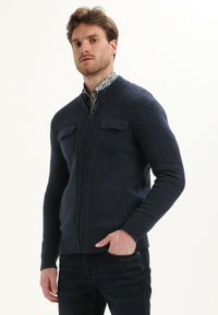 Maglione zip-up blu navy con colletto e polsini a coste, due tasche sul petto e tasche laterali, realizzato in tessuto a maglia testurizzata.