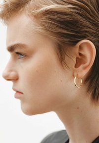 Un pendiente de aro dorado en una persona con cabello corto, mostrado de perfil. El pendiente es circular y pulido, creando un contraste con la piel clara.