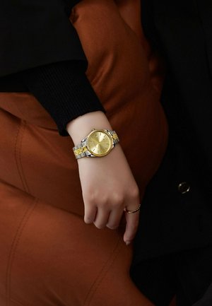Montre-bracelet en or et en argent avec un cadran rond, un cadran texturé et un affichage de la date. Le bracelet en métal présente des maillons alternés en or et en argent.