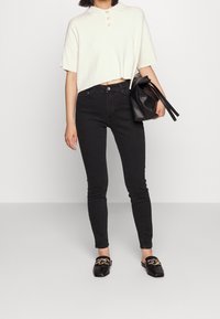 Krämfärgad kortärmad polo med knappar, svarta skinny jeans och svart läderväska med fransar. Svarta loafers med en guldkedjedetalj.