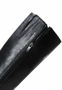Black leather bag with a smooth texture, angled zip closure, and a tapered design. Features a flat, wide base and minimal hardware.