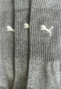 Graue Sportsocken aus geripptem Material, mit einem kleinen weißen Puma-Logo auf jeder Socke, mit glatter Textur und Standardform.