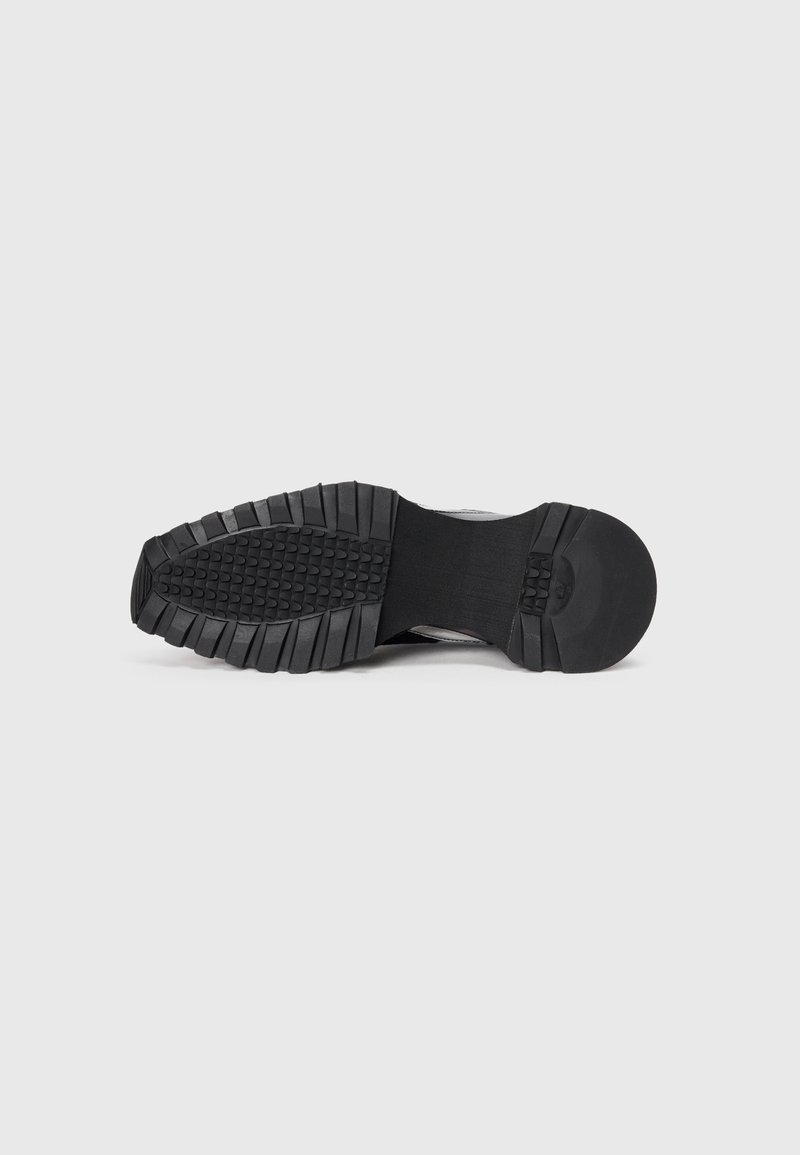 Zwarte sneaker outsole met een robuust looppatroon, voorzien van getextureerd rubber voor grip en flexibiliteit. Gladde tussenzool voor ondersteuning.