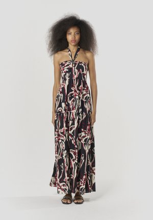 Sukienka maxi w czerni z abstrakcyjnym wzorem w kolorze czerwonym i kremowym, bez ramiączek, z lekkiego materiału, z wielowarstwowymi falbanami, zestawiona z czarnymi, płaskimi sandałami.