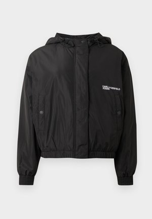 Melna saīsināta bumbvedēja jaka no neilona ar kapuci, elastīgiem aprocēm, regulējamu jostasvietu ar aukliņu un reljefa logotipu augšējā kreisajā pusē.