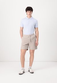 Camisa polo de color azul claro, pantalones cortos beige a rayas con cintura elástica y zapatillas blancas con detalles en negro. Conjunto simple y casual.