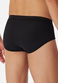 Culotte en coton noir avec une texture lisse, présentant une ceinture élastique noire unie avec logo, conçue pour un ajustement confortable.
