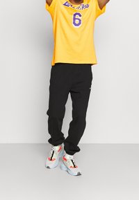 Żółta koszulka z krótkim rękawem z napisem "Lakers" i numerem "6" w kolorze fioletowym, zestawiona z czarnymi spodniami i kolorowymi butami sportowymi z teksturowaną podeszwą.