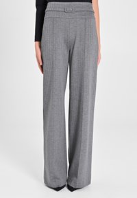 Pantaloni grigi a gamba larga con un tessuto testurizzato, strisce verticali e una vita alta con cintura. Presentano un design sartoriale e una silhouette fluida.