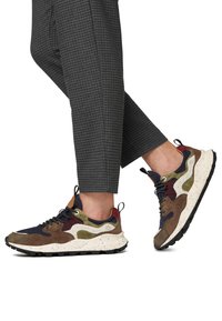 Sneaker multicolore caratterizzato da materiali in suede e mesh, una suola spessa bianca con macchie e un mix di accenti blu scuro, marrone e verde.
