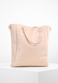 Jasnoróżowa torba typu tote wykonana z gładkiej skóry, z dwoma krótkimi uchwytami i złotym metalowym wykończeniem. Kwadratowy kształt o minimalistycznym designie.