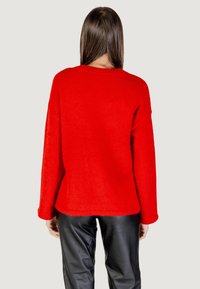 Maglione in pile rosso con maniche lunghe, vestibilità rilassata e scollo rotondo. Abbinato a pantaloni in pelle nera. Texture morbida, senza motivi visibili.