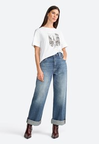 Hvid bomulds t-shirt med grafisk print, parret med vide blå denim jeans, opbrettede ærmer og brune ankelstøvler.