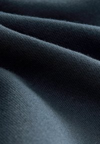 Tela azul oscura con una superficie suave y texturizada. Presenta patrones de punto finos y una apariencia lisa con sutiles variaciones en el tono.