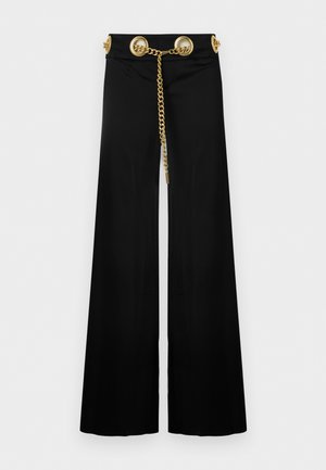 Black wide-leg pants with high waist featuring large gold eyelets and a gold chain belt threaded through them.