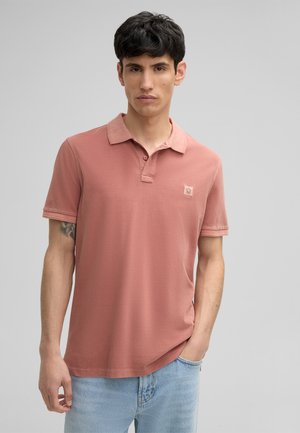Polo shirt en rose pâle, manches courtes, en coton doux, col, petite écusson logo sur la poitrine, associé à un jean en denim bleu clair.