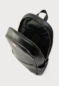 Čierny kožený batoh s vnútrom v tvare diamantového vzoru. Má prednú kapsu na zips a hlavný priestor s dvojcestným zipsom.