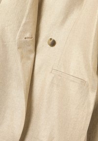 Blazer de lino beige con un solo botón, solapas puntiagudas y un bolsillo en el pecho izquierdo, con textura suave y un sutil brillo.