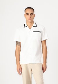 Short-sleeve white shirt with black trim on collar and pocket. Button-down front, lightweight fabric, casual design, featuring a single pocket.