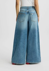Jeans in denim a gamba larga con un lavaggio blu chiaro sbiadito, cinque tasche e orlo grezzo. Presentano una vita con logo e una vestibilità ampia.