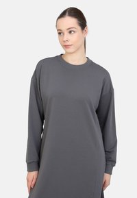 Graues, oversized Sweatshirtkleid mit langen Ärmeln, Rundhalsausschnitt und gerippten Bündchen. Glattes Kleidungsstück mit minimalen Nähten und ohne sichtbare Muster.