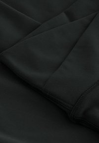 Tissu noir avec coutures visibles et plis qui se chevauchent, montrant une texture lisse et des reflets subtils de lumière.