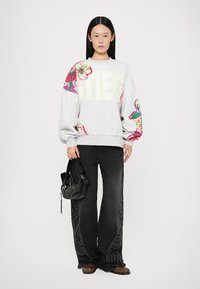 Gray sweatshirt with floral embroidery and "STIEG" lettering, paired with wide-leg black jeans featuring detailed stitching. Model holding a black bag.