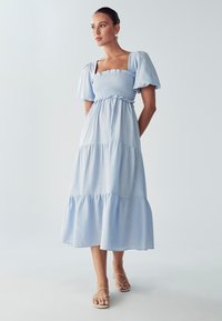 Svetlo modra midi obleka s napihnjenimi rokavi, smučastim trupom in plastehnim volančkom na robu. Narejena iz mehkega blaga z gladko teksturo.