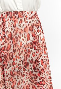 Gonna leggera e trasparente con una stampa leopardata rossa e marrone su uno sfondo chiaro, con una consistenza liscia e una vita elastica.