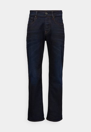 Jean en denim bleu foncé avec une coupe droite, cinq poches et des détails de coutures contrastants. Le matériau a une texture lisse et tissée.