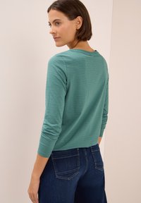 Teal striped long-sleeve top with a rounded neckline, paired with dark blue jeans. The fabric appears soft and has a smooth texture.