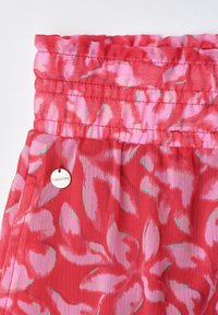Jupe à motif floral rouge et rose avec taille élastique smockée et petite étiquette métallique ronde de la marque près de la poche.