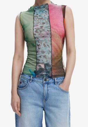 Haut sans manches avec des panneaux verticaux multicolores en vert, bleu, rose et marron, porté avec un jean bleu clair, une main dans la poche.