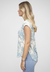 Haut bleu clair à fleurs avec manches courtes, coupe décontractée et ourlet arrière plus long, confectionné dans un tissu doux et texturé.