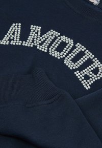 Námořnická modrá mikina s textovým designem "AMOUR" vyrobeným z lesklých kamínků. Hladké manžety a výstřih dodávají texturu a detaily.