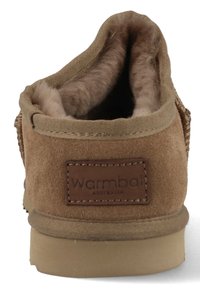 Brown suede slipper featuring a soft, fuzzy interior lining, a tan rubber sole, and a rectangular leather label with embossed brand name.