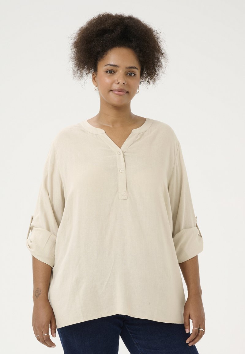 Beige Hemd mit Knopfleiste und V-Ausschnitt, drei Viertelärmel mit umgeschlagenen Bündchen. Weicher, leichter Stoff mit lässiger Passform.