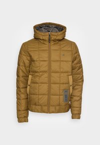 Brun vadderad puffer-jacka med huva, framdragkedja, elastiska ärmmuddar, två sidofickor med knappflikar och en liten logotyp på bröstet.