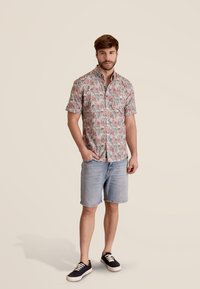 Korte mouwen knoopshirt in lichtroze met een groen en blauw bloemmotief. Gecombineerd met lichte denimshorts en donkere sneakers.