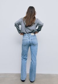 Svetlomodré rifle s vysokým pásom a rovnými nohavicami, s tmavým pásom a nášivkou. Nosí sa s šedou dlhou rukávovou košeľou.