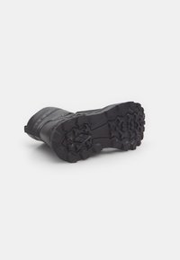 Cizmă neagră impermeabilă cu un outsole din cauciuc texturat, având caneluri adânci pentru aderență și o guleră îmbrăcată pentru confort.